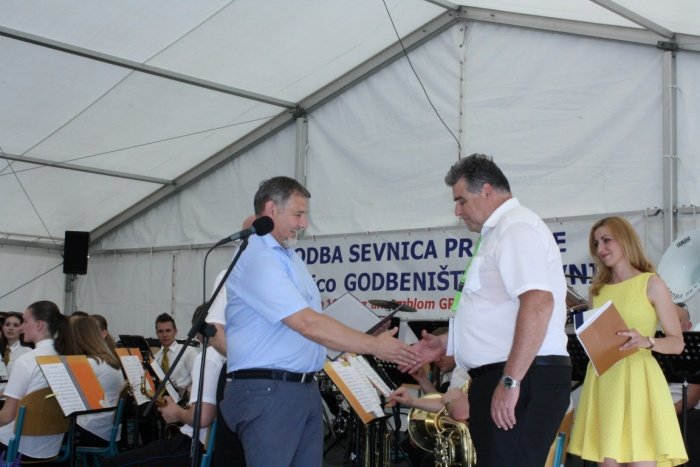 Godbi je župan Srečko Ocvirk (levo) izročil listino občine Sevnica, ki jo je sprejel predsednik godbe Janez Šerjak. Program je povezovala Tanja Žibert (desno). (Foto: M. L.)