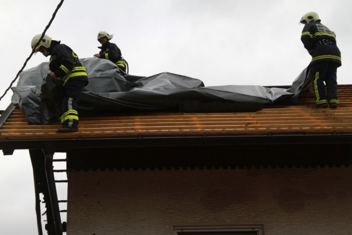 Gasilci nameščajo zaščitno folijo na en del strehe. 