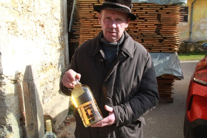 Ivan Škarja s steklenico domačega žganja, v njej pa so miniaturne mojstrovine.